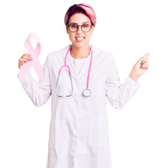 Canvas Print - Young beautiful woman with pink hair wearing doctor stethoscope holding cancer ribbon smiling happy pointing with hand and finger to the side