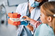  Children's dentistry. Cropped image of a nurse holding a mockup of a jaw with teeth and a child patient showing her brushing her teeth on the mockup.