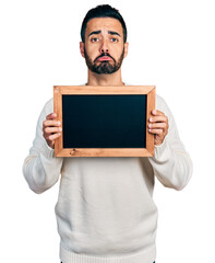 Sticker - Young hispanic man with beard holding blackboard depressed and worry for distress, crying angry and afraid. sad expression.