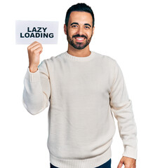 Wall Mural - Young hispanic man with beard holding lazy loading banner looking positive and happy standing and smiling with a confident smile showing teeth