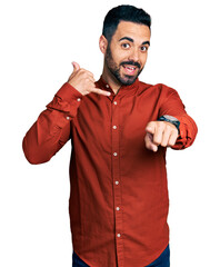 Wall Mural - Young hispanic man with beard wearing casual shirt smiling doing talking on the telephone gesture and pointing to you. call me.