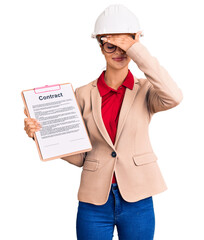 Poster - Young beautiful woman wearing architect hardhat holding clipboard with contract document stressed and frustrated with hand on head, surprised and angry face