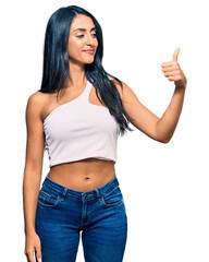 Wall Mural - Beautiful hispanic woman wearing casual clothes looking proud, smiling doing thumbs up gesture to the side