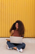 © ADDICTIVE STOCK - Cheerful African American self employed woman sitting on street with laptop