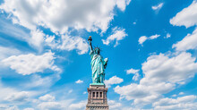 Vivid Image Of The Statue Of Liberty In The Daytime, Blue Sky With White Fluffy Clouds In The Background, Captured From A Low Angle