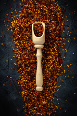 Wall Mural - Dried red pepper flakes with wooden spoon isolated on dark background. Top view