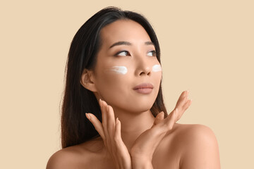 Sticker - Beautiful young Asian woman with cream on her face against beige background