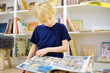 © Maria Sbytova - A preteen boy leafing through a book while sitting at the bookshelves at home, in a school library or bookstore. Smart kid reading comics
