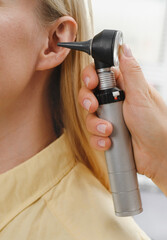 Woman patient having check-up of hearing at doctor otolaryngologist. Hearing exam for female. Otolaryngologist doctor checking mature woman's ear using otoscope or auriscope at medical clinic