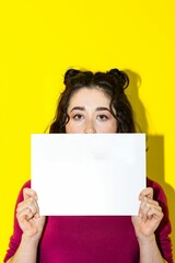 young woman holding and hiding her face on a poster. Girl holding a blank poster on isolated background