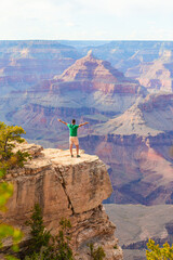 Young hiker is standing on a steep cliff taking in the amazing view over famous Grand Canyon on a beautiful sunny day with blue sky in summer, Grand Canyon National Park, Arizona, USA