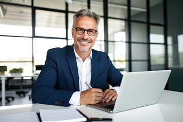Smiling mature adult business man executive sitting at desk using laptop. Happy busy professional mid aged businessman ceo manager working on computer corporate technology in office