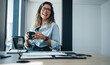 © Jacob Lund - Professional business woman sitting in an office, smiling and holding a cup of coffee