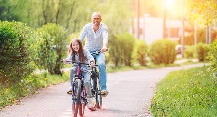 portraits smiling father with daughter during summer outdoor bicycle riding. they enjoy togetherness