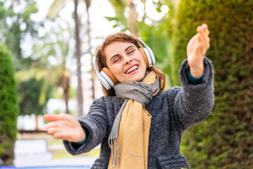 Wall Mural - Brunette woman listening music with headphones at outdoors presenting and inviting to come with hand