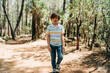 Tourist school boy kid child in a casual clothing walking in the summer greenwood leaf forest with rocky boulders stones all around the place