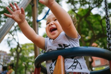 Close up of baby girl playing on outdoor playground swing. Toddler playing on school or kindergarten yard. Active kid on colorful swing. Healthy summer activity for children outdoors