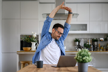 Wall Mural - Tired male entrepreneur stretching arms while working overtime on laptop at desk in home office