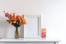 White Empty Frame For A Picture Or Artwork On The Table, With Lovely Orange Pink Flowers In A Glass Vase Close By. Generative AI
