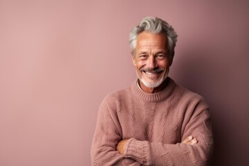 Wall Mural - Environmental portrait photography of a happy mature man wearing a cozy sweater against a dusty rose background. With generative AI technology