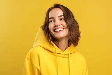 Wall Mural - Medium shot portrait photography of a grinning girl in her 20s wearing a comfortable hoodie against a bright yellow background. With generative AI technology