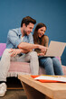 © Jose Calsina - Vertical portrait of young couple watching the laptop screen, checking finances, planning budget or mortgage sitting at couch. Smiling husband showing on his wife's notebook a online shopping sale