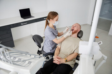 Portrait of young female dentist standing by mid adult man in clinic. Female dentist repairing patient tooth in dental ambulant