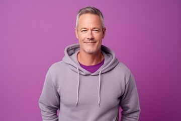 Wall Mural - Medium shot portrait photography of a beautiful mature man wearing a cozy zip-up hoodie against a lilac purple background. With generative AI technology
