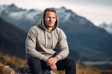 Wall Mural - Sports portrait photography of a glad boy in his 30s wearing a stylish hoodie against a mountain range background. With generative AI technology