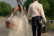 Close up of young newlywed couple holding  suitcases of cash on countryside road
