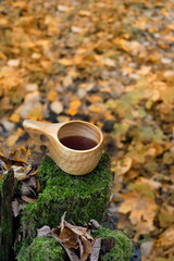 Wall Mural - wooden cup with tea on mossy stump in autumn forest, blurred natural background. Traditional Finnish mug 