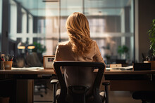 A Women Sitting In A Chair In Front Of A Desk In An Office, Back View