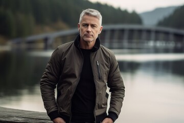 Wall Mural - Lifestyle portrait photography of a tender mature man wearing a sleek bomber jacket against a tranquil lake background. With generative AI technology