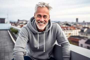 Wall Mural - Urban fashion portrait photography of a joyful mature man wearing a comfortable hoodie against a rooftop terrace background. With generative AI technology