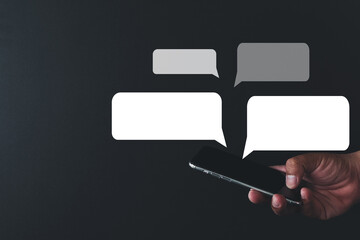 Hand holding smartphone with speech bubbles icon over black background perfect for technology,chat message,group chat,Texting,e-maill,internet idea.