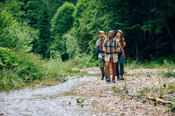multiracial group of hikers walking by mountain creek.