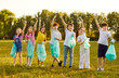 © Studio Romantic - Group of cheerful and active volunteer children gathered together to clean up litter-polluted park. Children stand in row in open with garbage bags in their hands and wave happily looking at camera.