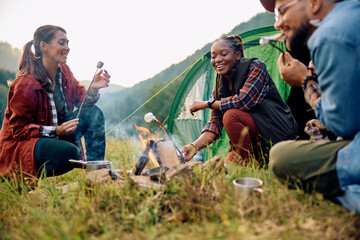 Young happy hikers roasting marshmallows on camping day in nature.