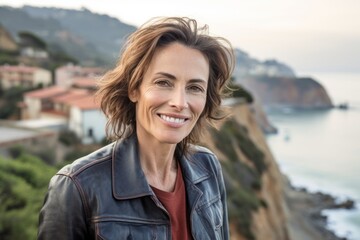 Wall Mural - Headshot portrait photography of a grinning mature woman wearing a denim jacket against a scenic cliffside village background. With generative AI technology
