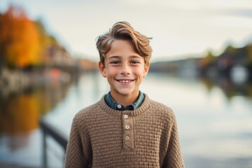 Wall Mural - Headshot portrait photography of a happy mature boy wearing a cozy sweater against a peaceful riverside walk background. With generative AI technology