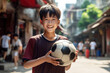 © zakiroff - Asian boy is staying on a asian street background and holding his soccer ball