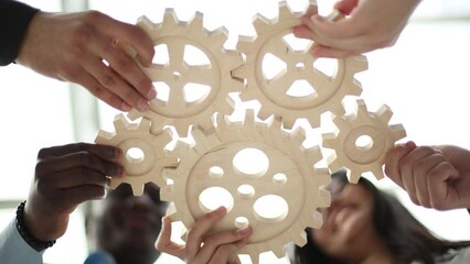 Wall Mural - Business people holding wooden gears in the office, bottom view