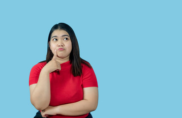 Wall Mural - Portrait girl young woman asian chubby fat cute beautiful pretty one person wearing a red shirt is sitting, looking, and thinking idea  suspiciously and seriously  isolated blue background