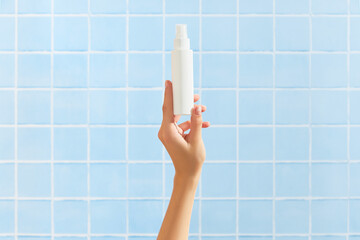 Poster - Womans hand holding white tube on blue tile background. Beauty treatment. Skin care routine