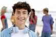 Portrait of smiling teenager with braces wearing headphones looking at camera standing on the street with friends on background. Summer concept