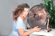 © Tatiana - woman holding air cooling fan smiles enjoying the wind from the blades in the apartment. Cooling the air in the summer heat