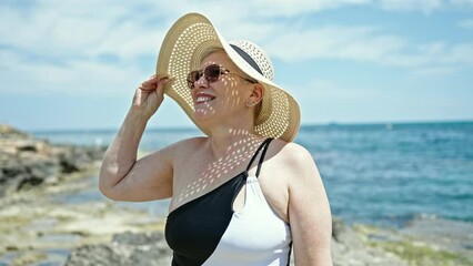 Canvas Print - Middle age grey-haired woman tourist wearing swimsuit and summer hat smiling at the beach