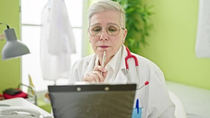 Poster - Middle age grey-haired woman doctor reading medical report thinking at clinic