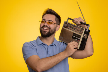 Happy excited man using retro tape record player to listen music, disco dancing of favorite track, having fun, entertaining, fan of vintage technologies. Handsome guy isolated on yellow background