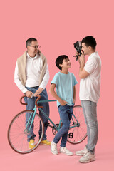 Wall Mural - Young man showing bike helmet to his little son and father on pink background